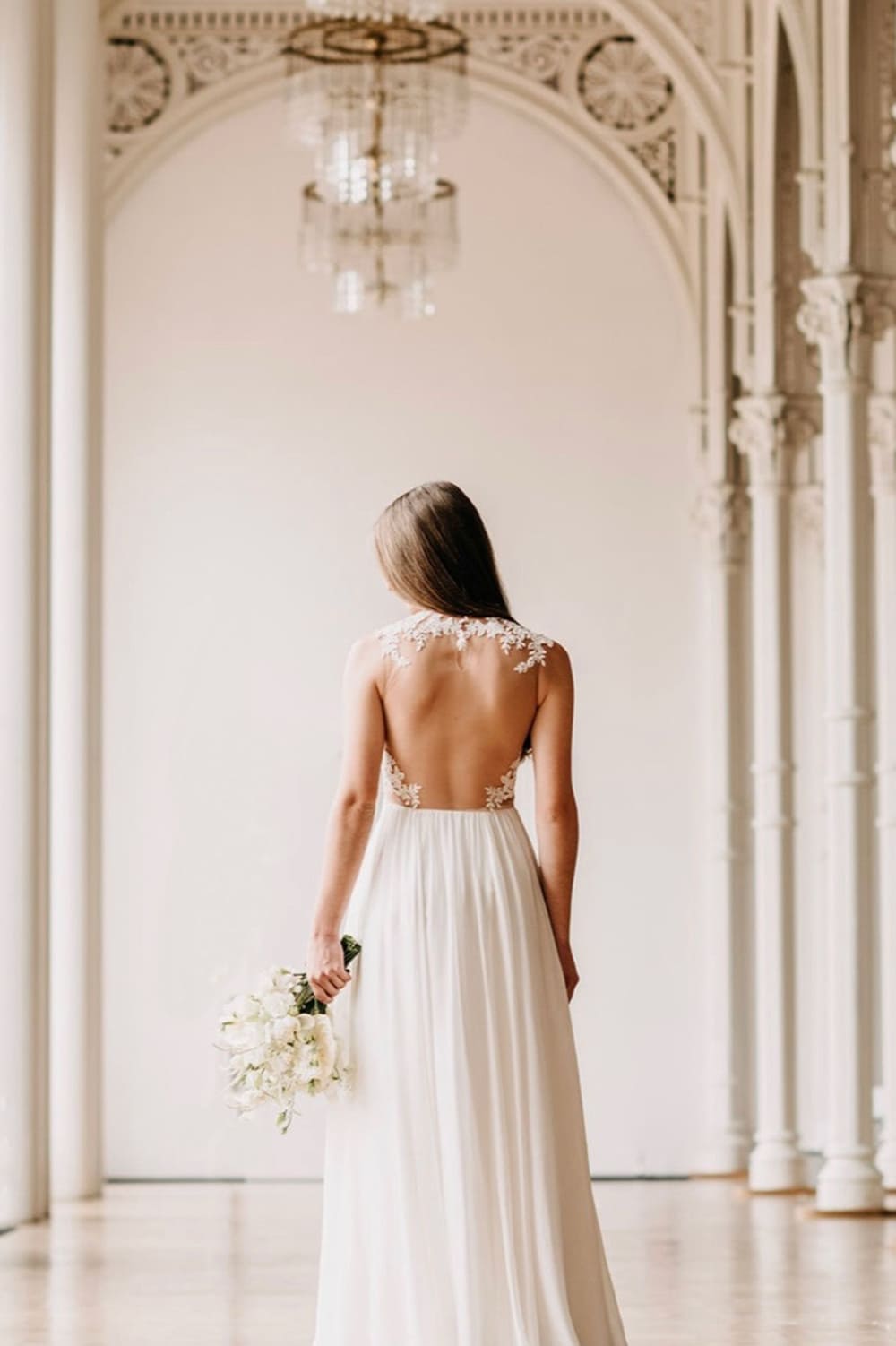 Rückansicht einer Braut mit Spitzen-Kleid und rotem Brautstrauß