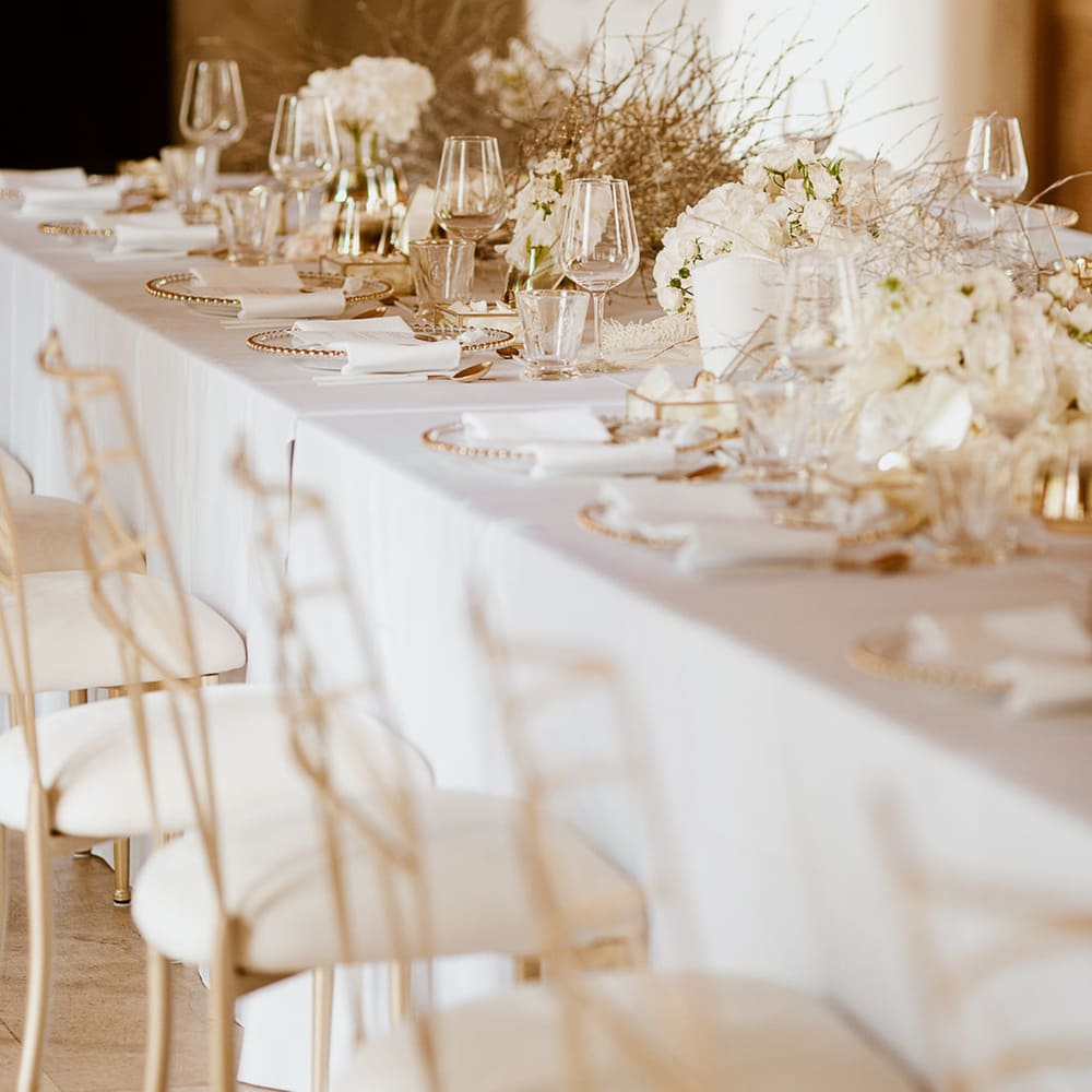 Gedeckte Tafel mit weißer Tischdecke, goldenen Stühlen und Dekoration und gebundenen Zweigen